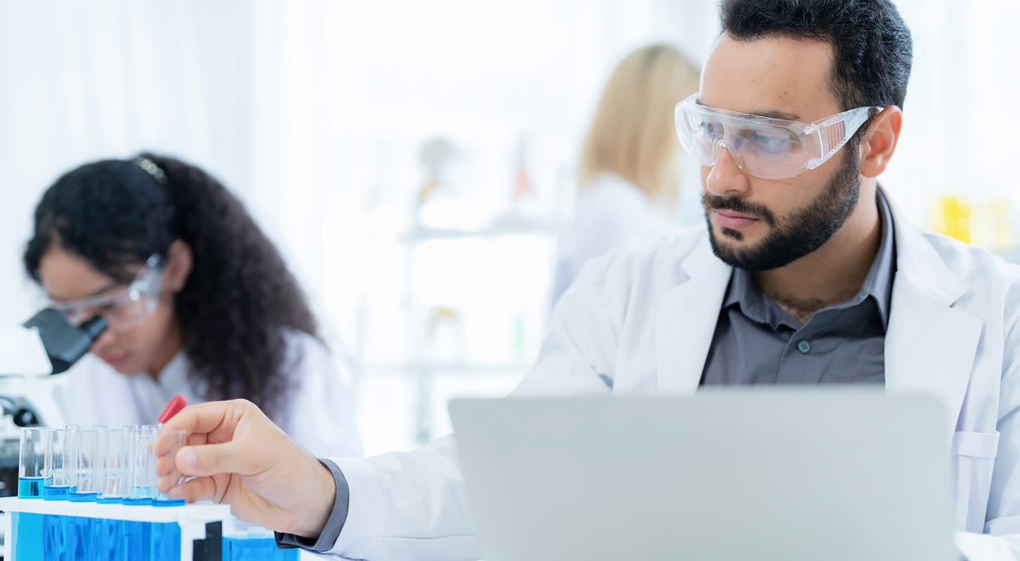 A man and woman in lab coats with safety goggles engaged in scientific research and analysis.